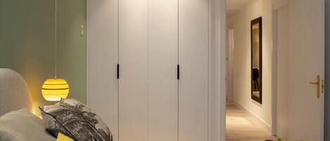 A bedroom with a bed, bedside lamps, a wardrobe, and a hallway leading to another room.