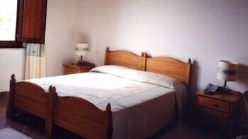A wooden bed with a white bedspread in a room with a window, a nightstand with a lamp, and a small table with a lamp.