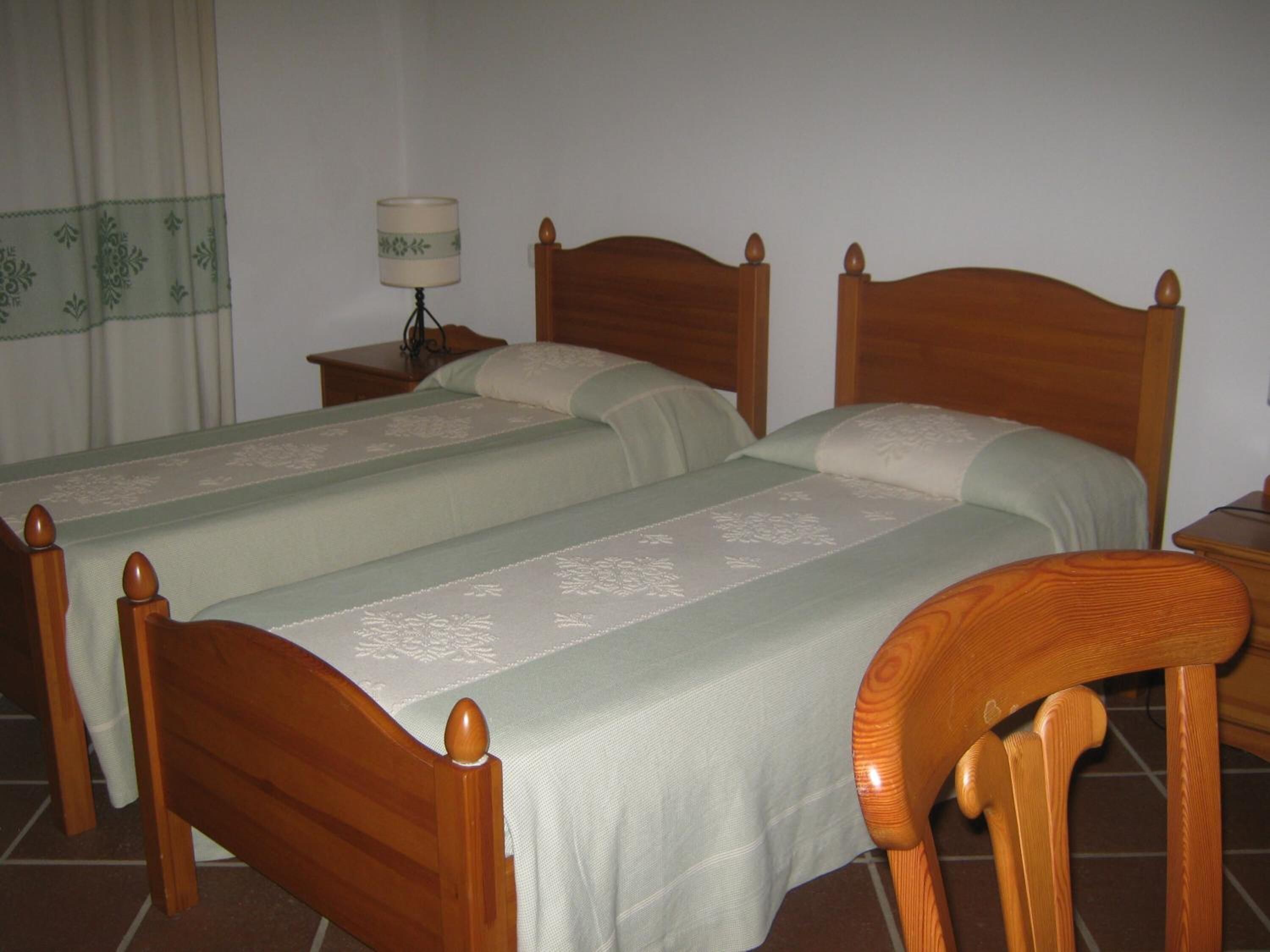 A room with two wooden beds, a nightstand with a lamp, and a window with curtains.