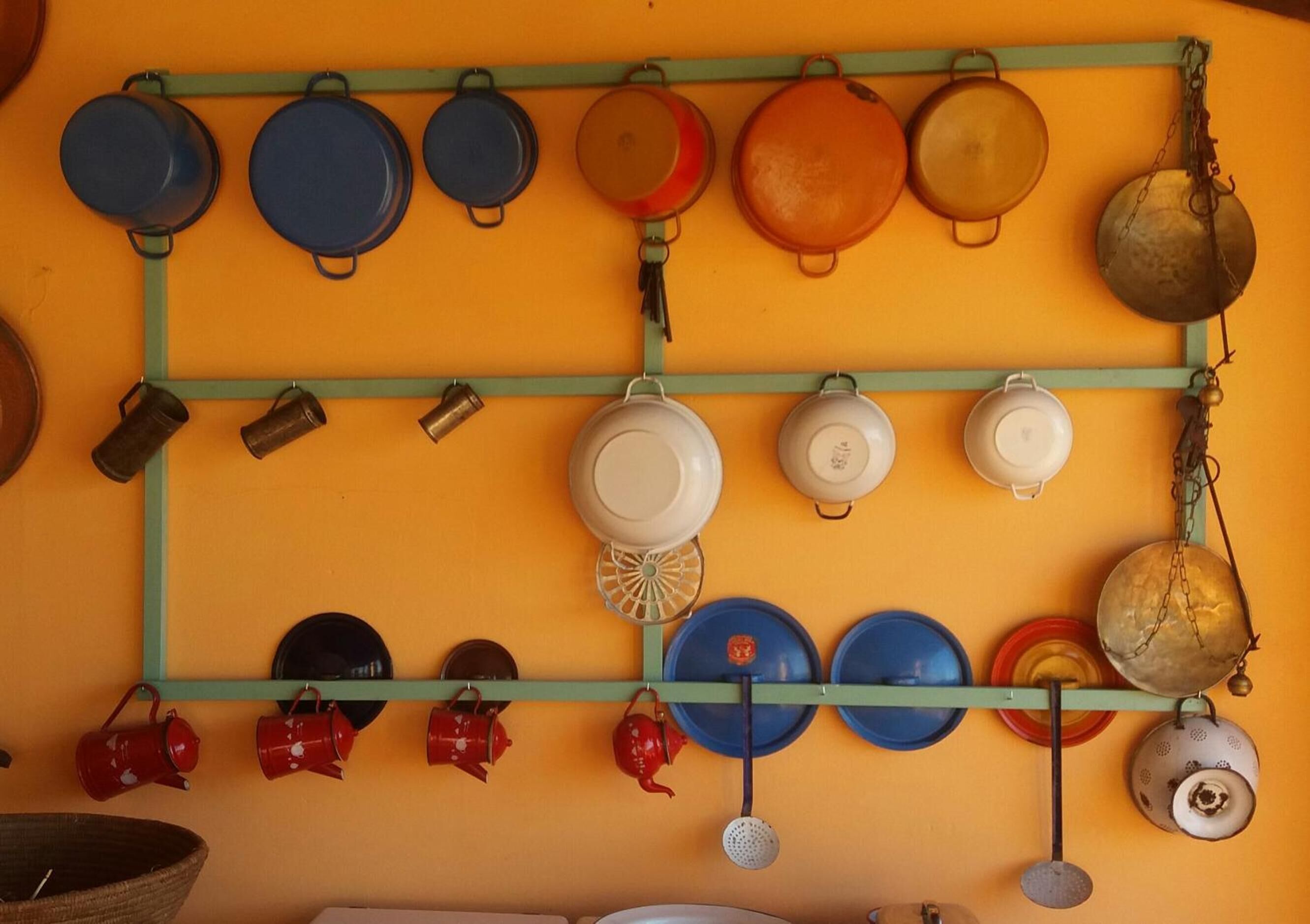 Une cuisine avec des casseroles et des poêles suspendues à un étagère contre un mur orange.