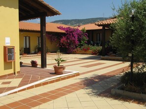 Une cour avec un sol carrelé, des plantes en pot et un bâtiment doté d’un toit en tuiles.