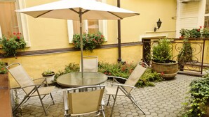 A patio with a round table and four chairs, surrounded by potted plants and flowers. - Hotel Heluan (Karlovy Vary)