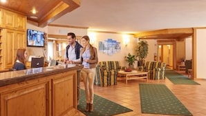 Un área de recepción con armarios de madera, mostrador y pantalla de televisión. Hay una zona de estar con un sofá y una mesa de centro.