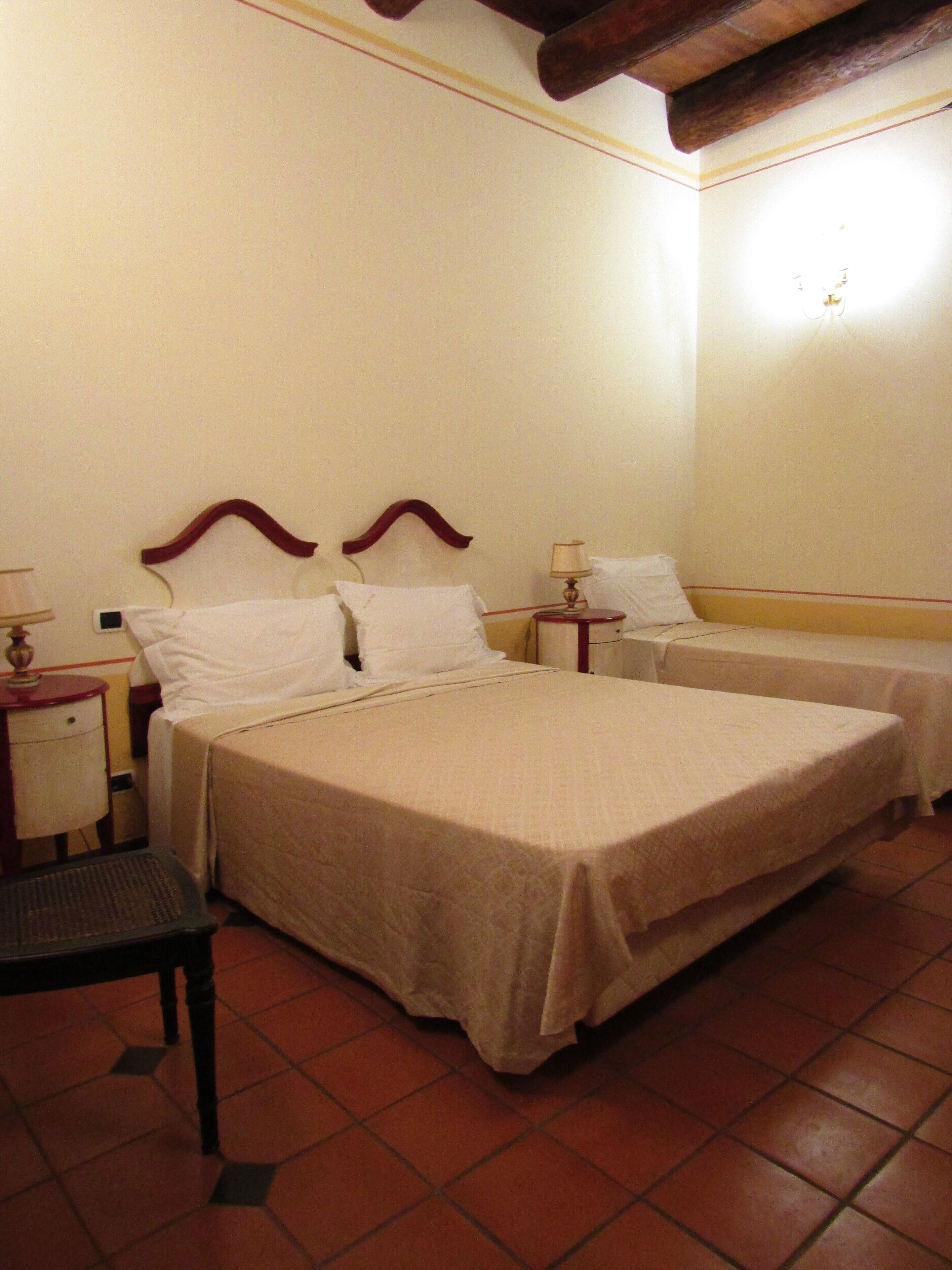A hotel room with two beds, a bedside table, a chair, and a lamp.