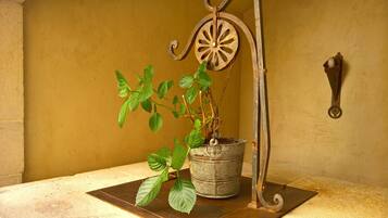 A potted plant with a rustic metal stand on a tiled floor against a yellow wall.