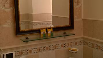 A bathroom with a white sink, a mirror with a gold frame, and a glass shelf below the mirror.