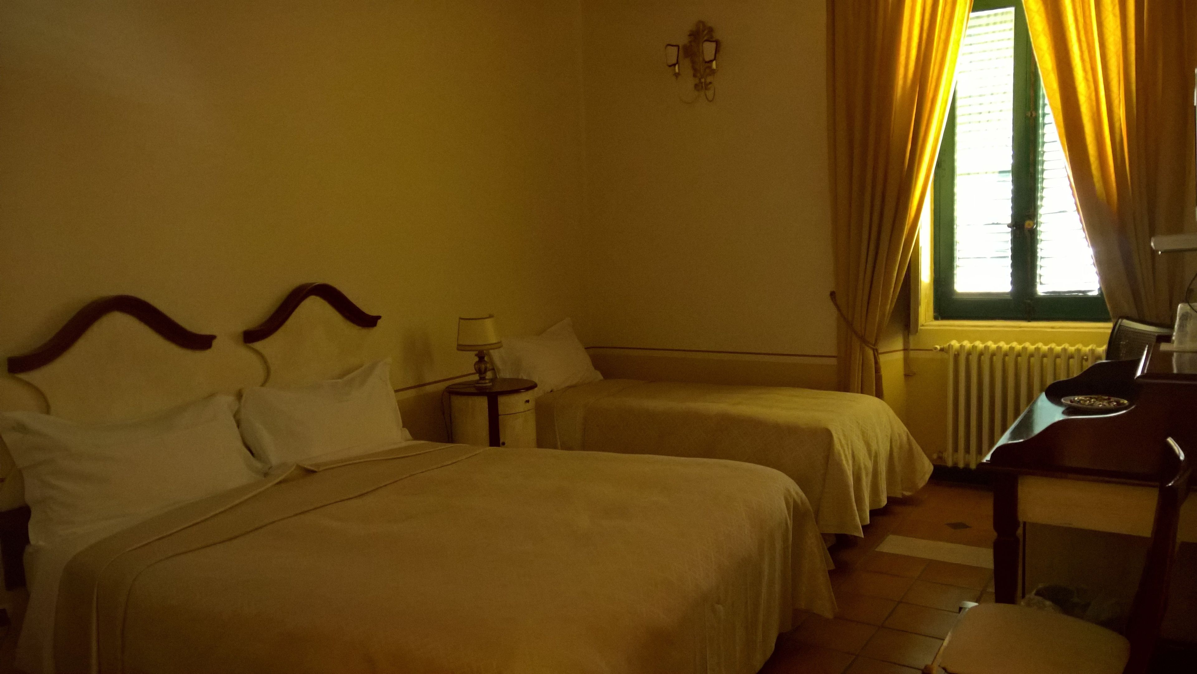 A hotel room with two beds, a nightstand, a desk, and a window with curtains.