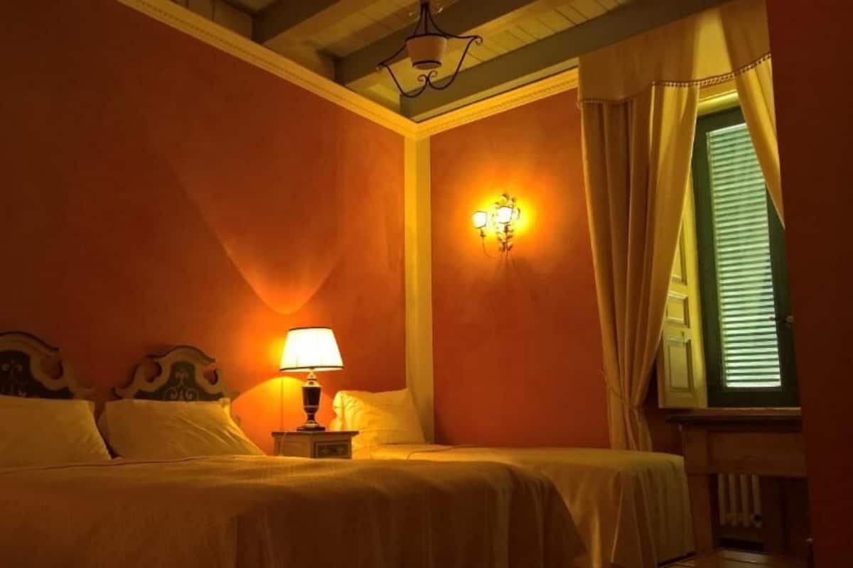 Un lit double avec une table de chevet et une lampe, un luminaire fixé au mur et une fenêtre avec des rideaux.