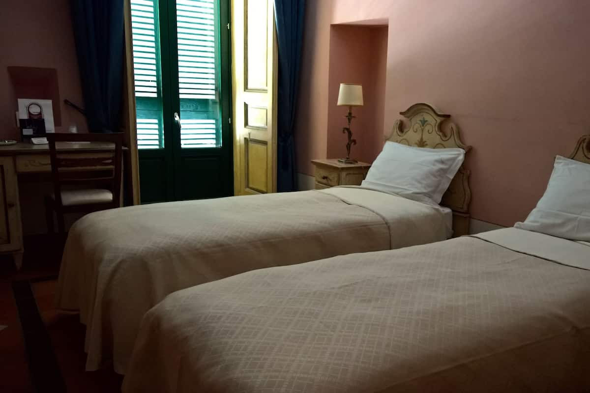 Une chambre avec deux lits, un bureau, une chaise, une lampe et une fenêtre avec des rideaux.