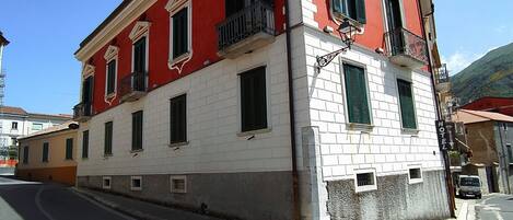 A two-story building with a red and white facade, multiple windows with shutters, and a balcony on the second floor.