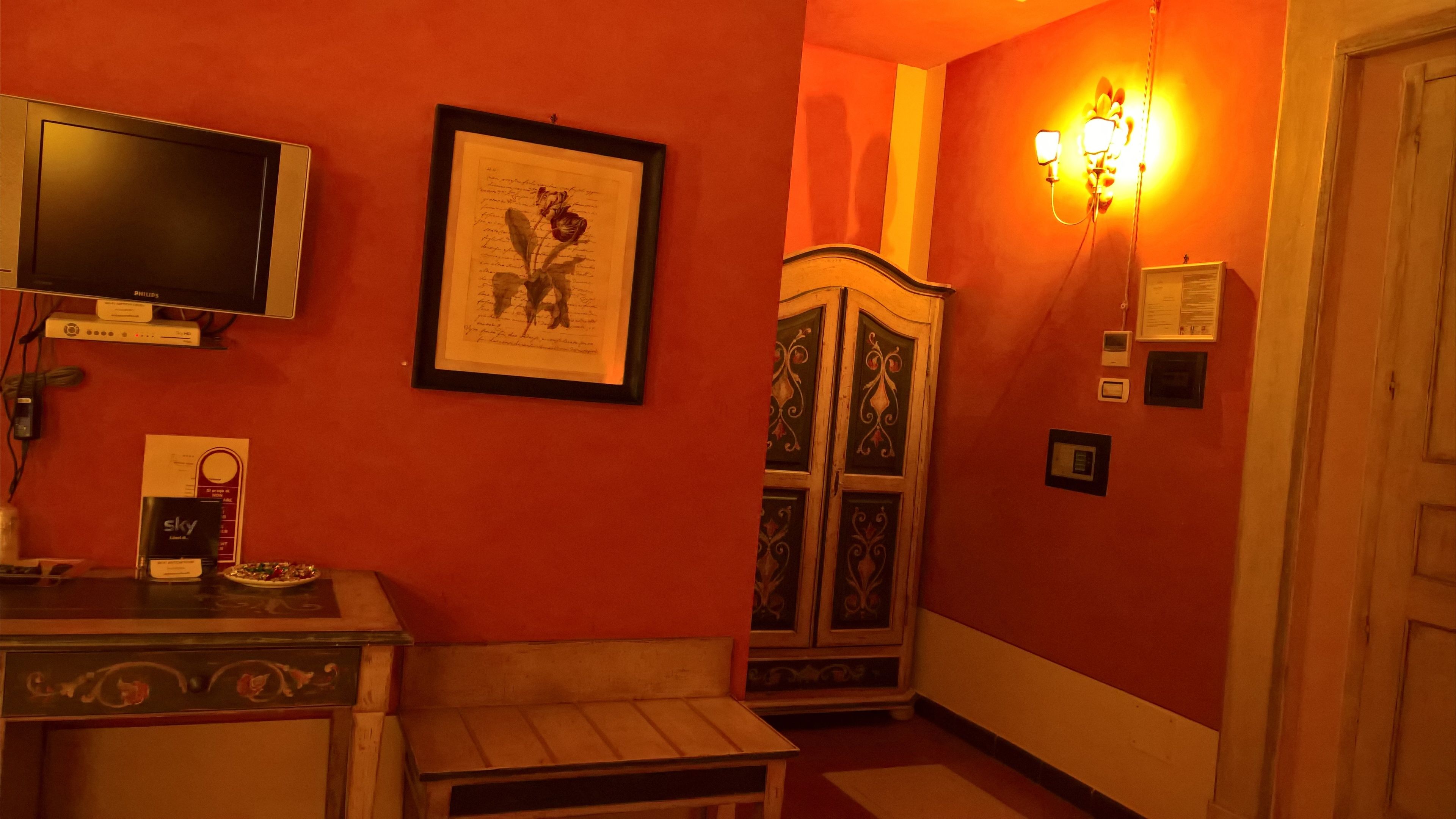 Una habitación con televisión, una obra de arte enmarcada, un armario y una lámpara de pared.