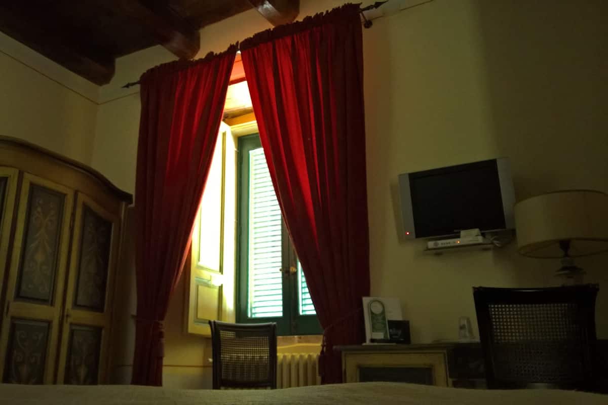 Une chambre à coucher avec un lit, un téléviseur fixé au mur et une fenêtre ornée de rideaux rouges.