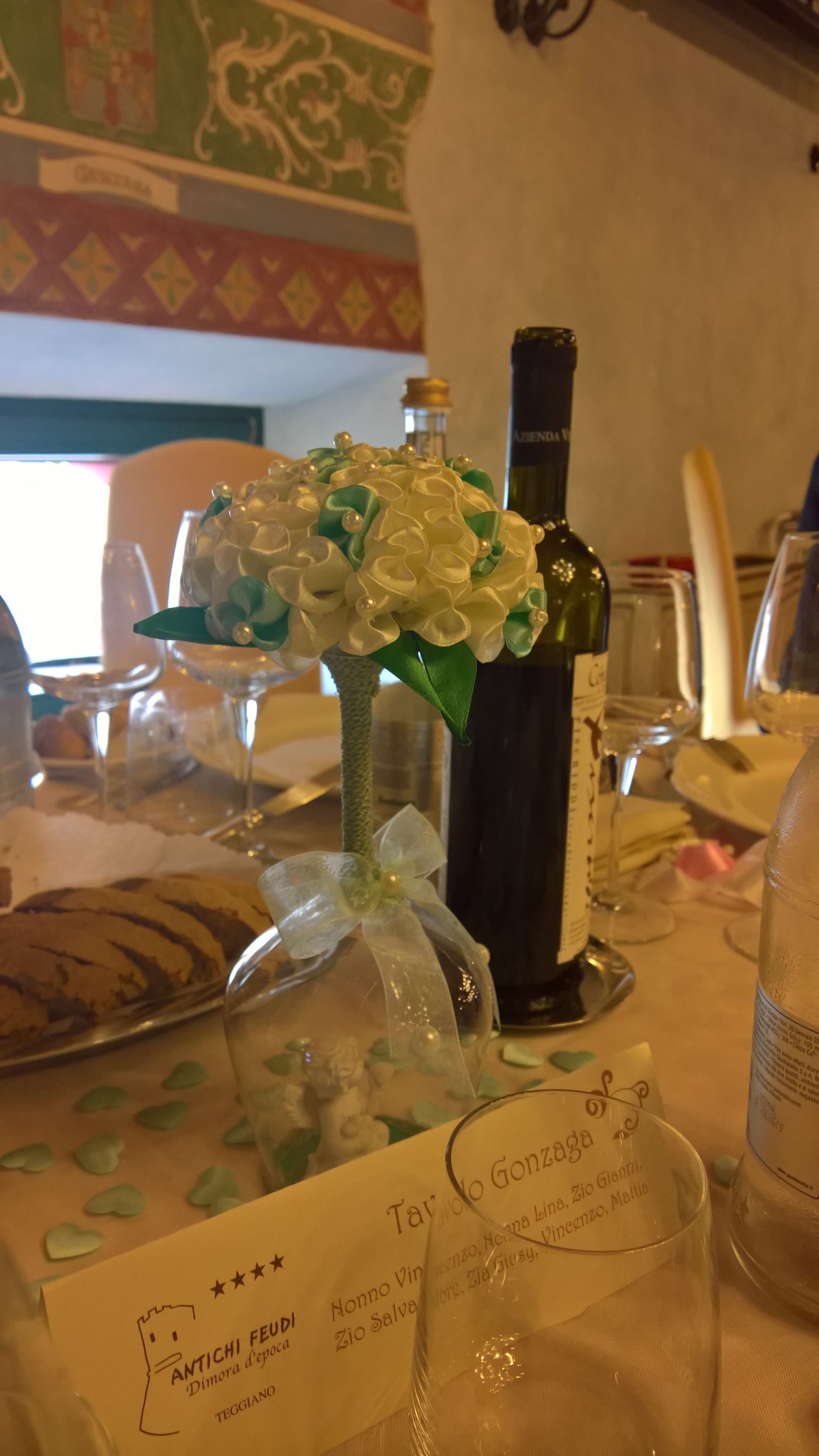 A table setting with a decorative vase, a bottle of wine, and a menu.