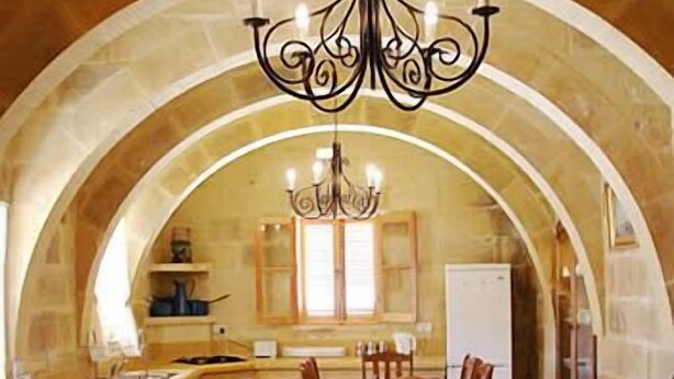 Une cuisine dotée d’un plafond en arc de cercle, d’un lustre, de meubles de rangement en bois et d’une table à manger avec des chaises.