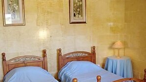Une chambre à coucher avec deux lits en bois, une petite table ronde avec une lampe et des tableaux encadrés accrochés au mur.