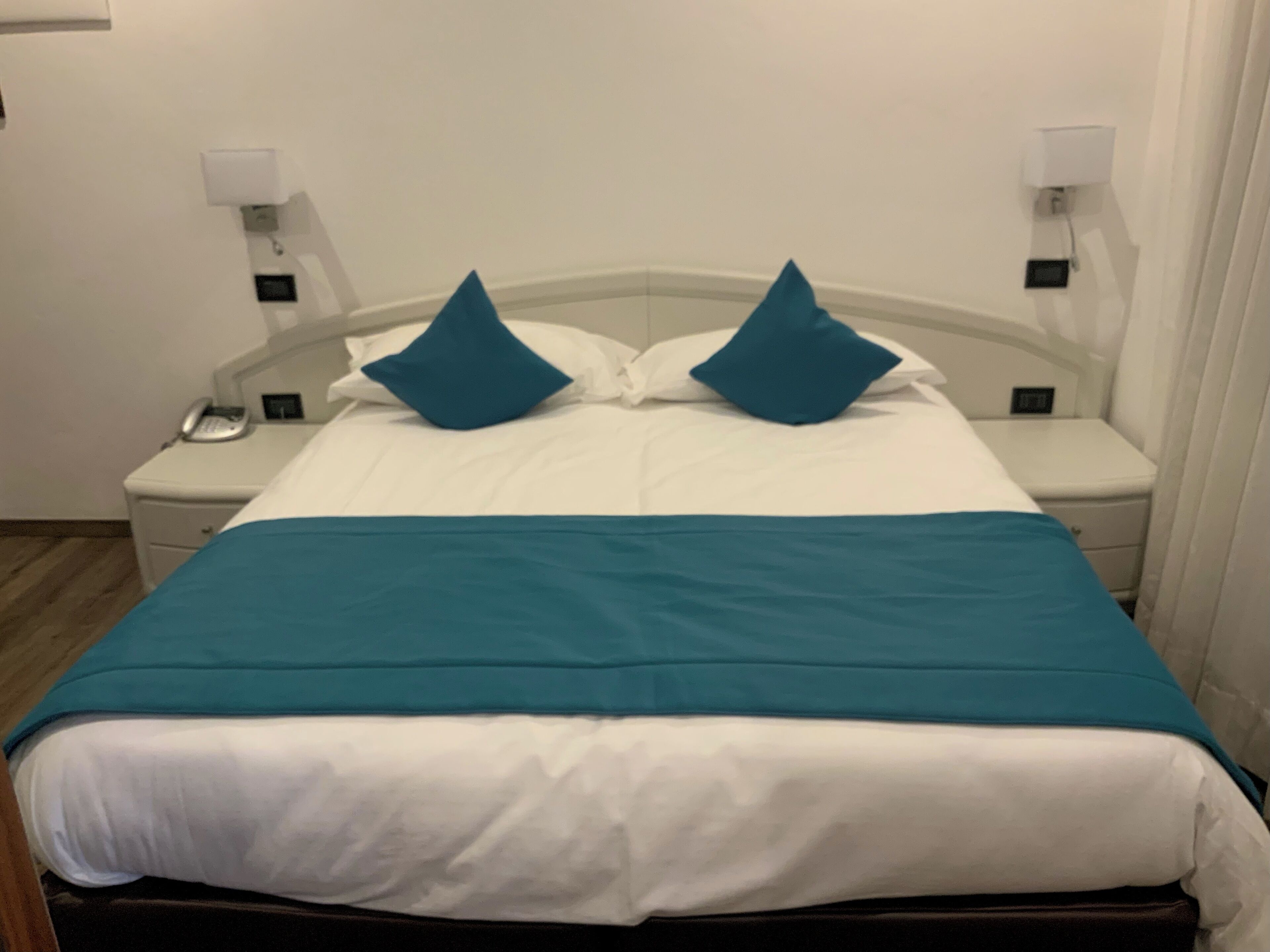 Una habitación de hotel con cama, paredes blancas y una pared azul decorativa.