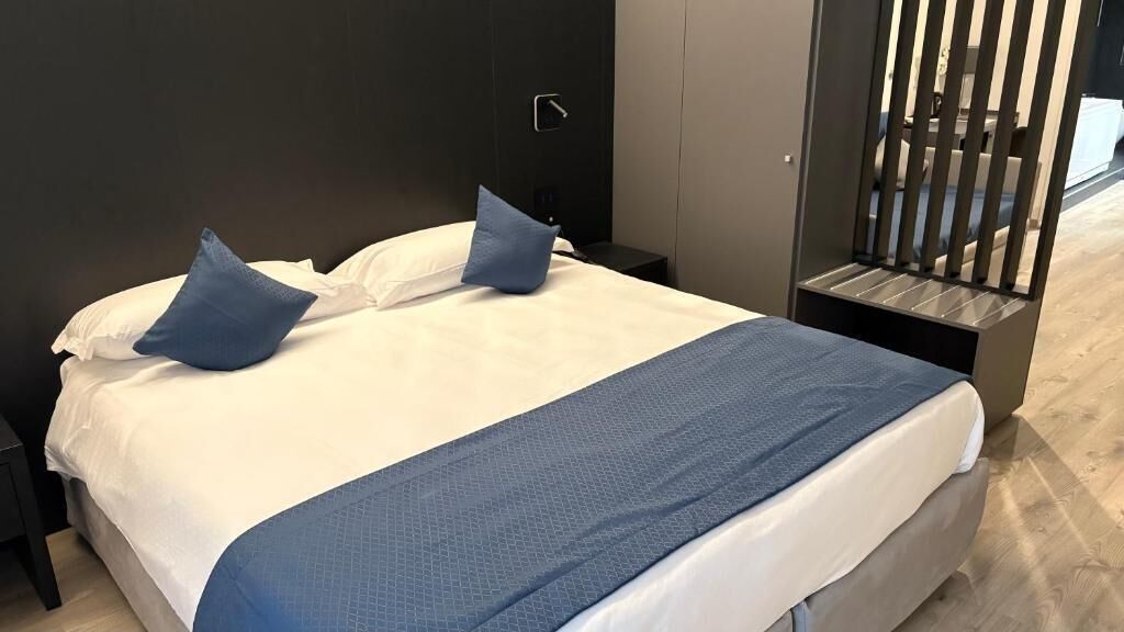 Ein modernes Hotelzimmer mit einem großen Bett, einem Nachttisch und einer integrierten Sitzbank mit Stauraum.