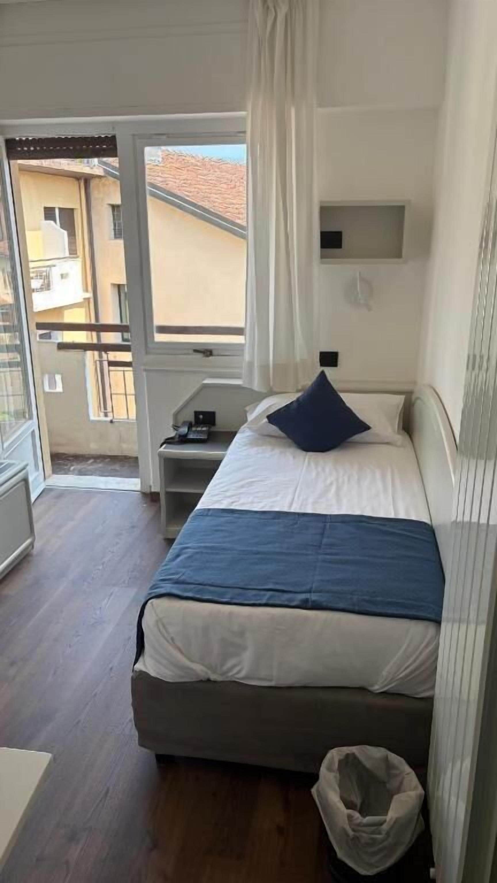 A bedroom with a bed, a bedside table, a chair, and a view of the outside.
