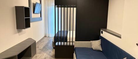 A modern hotel room with a bed, a small desk, a TV mounted on the wall, and a window with curtains.