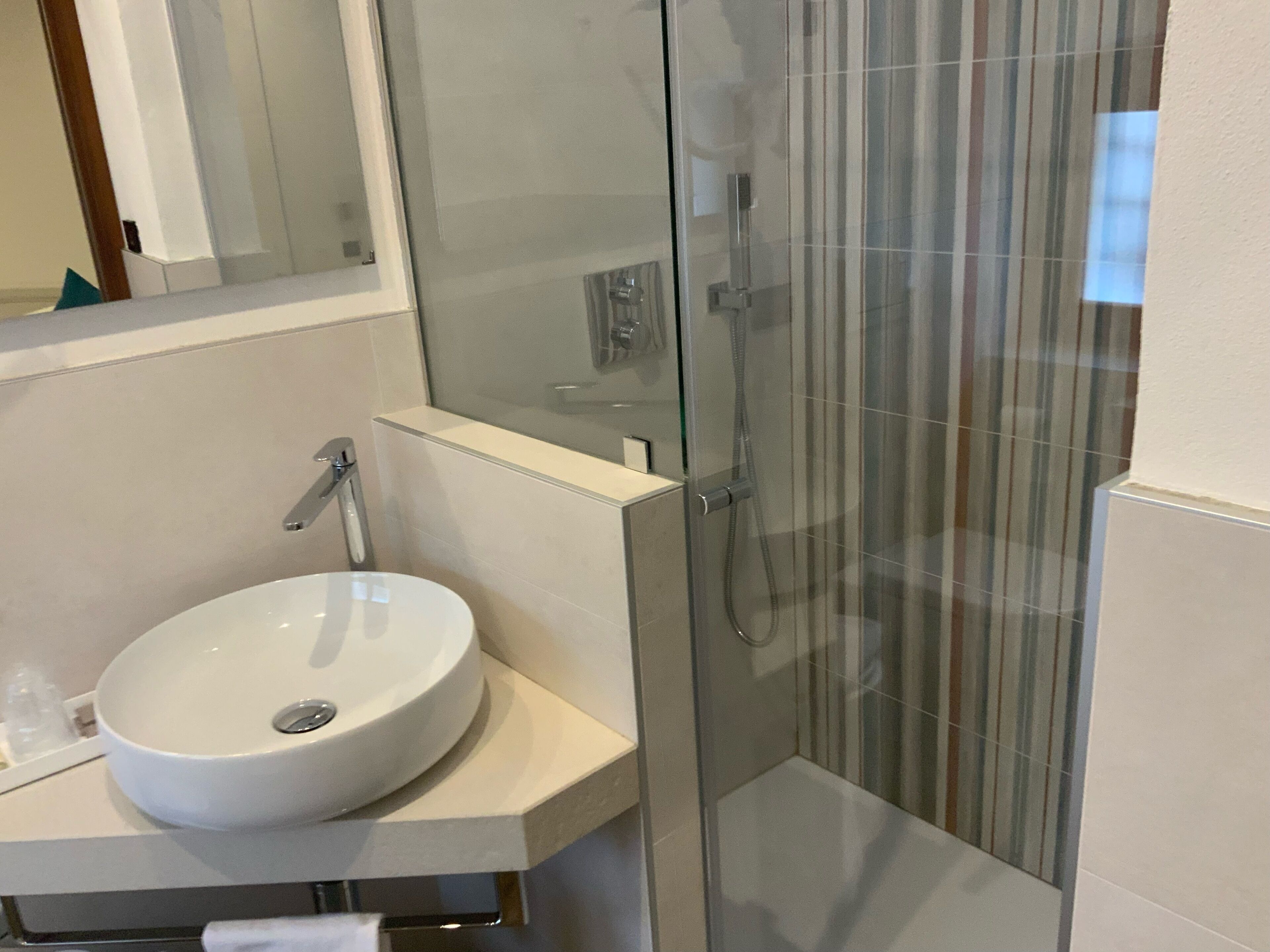 Un baño moderno con un lavamanos blanco, una cabina de ducha de vidrio y un espejo sobre el lavamanos.