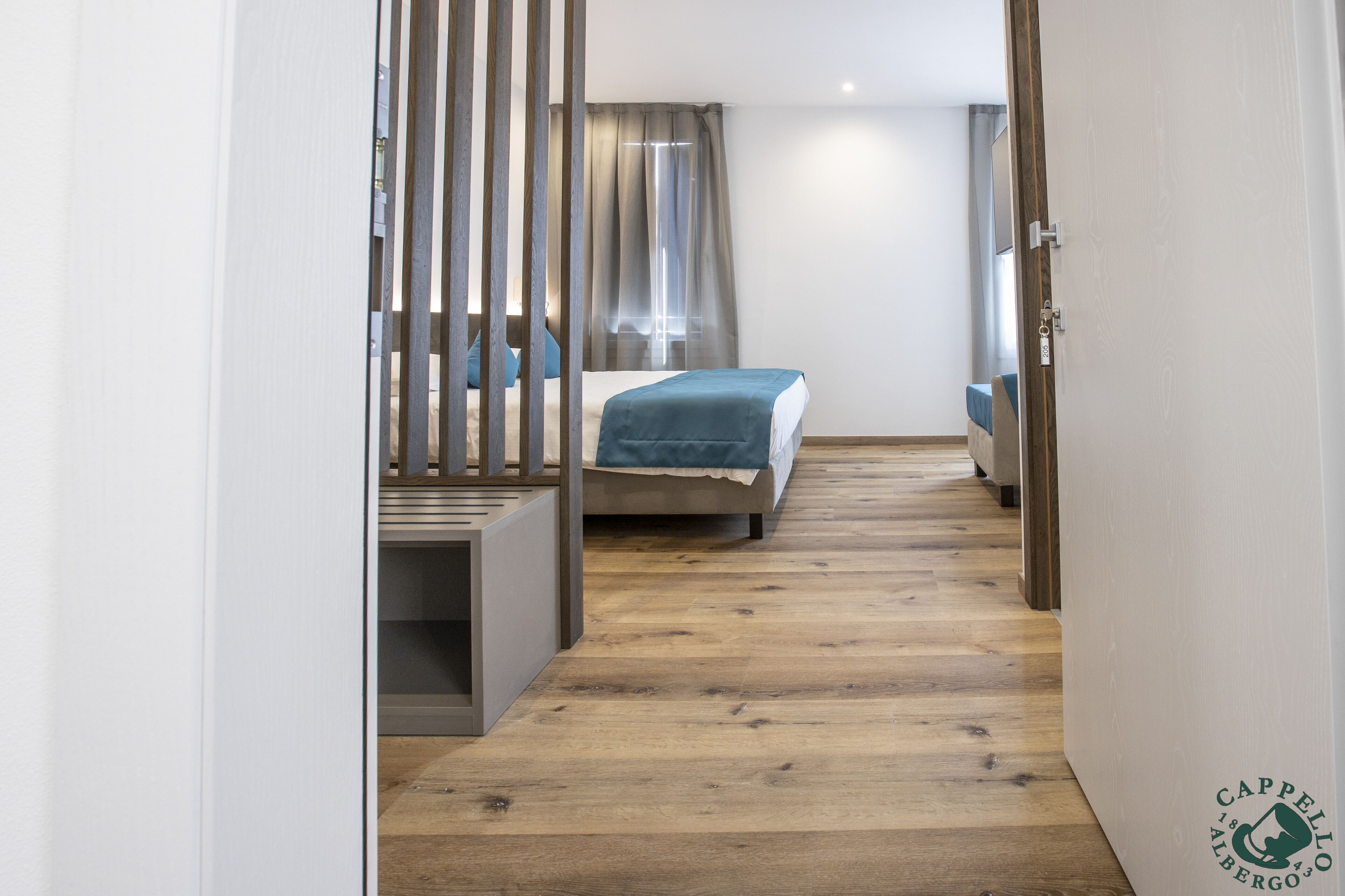A narrow hallway leading to a bedroom with a bed, a desk, and a window with curtains.