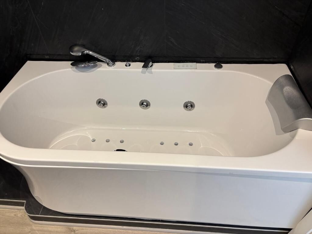 A white bathtub with a handheld showerhead and two faucets.