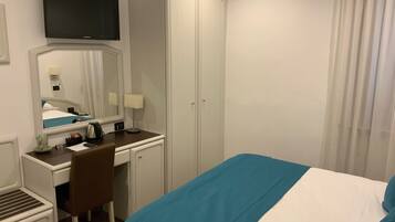 Ein Hotelzimmer mit einem Bett, einem Schreibtisch mit Stuhl, einem Kleiderschrank, einem Fernseher über dem Schreibtisch und einem Spiegel.