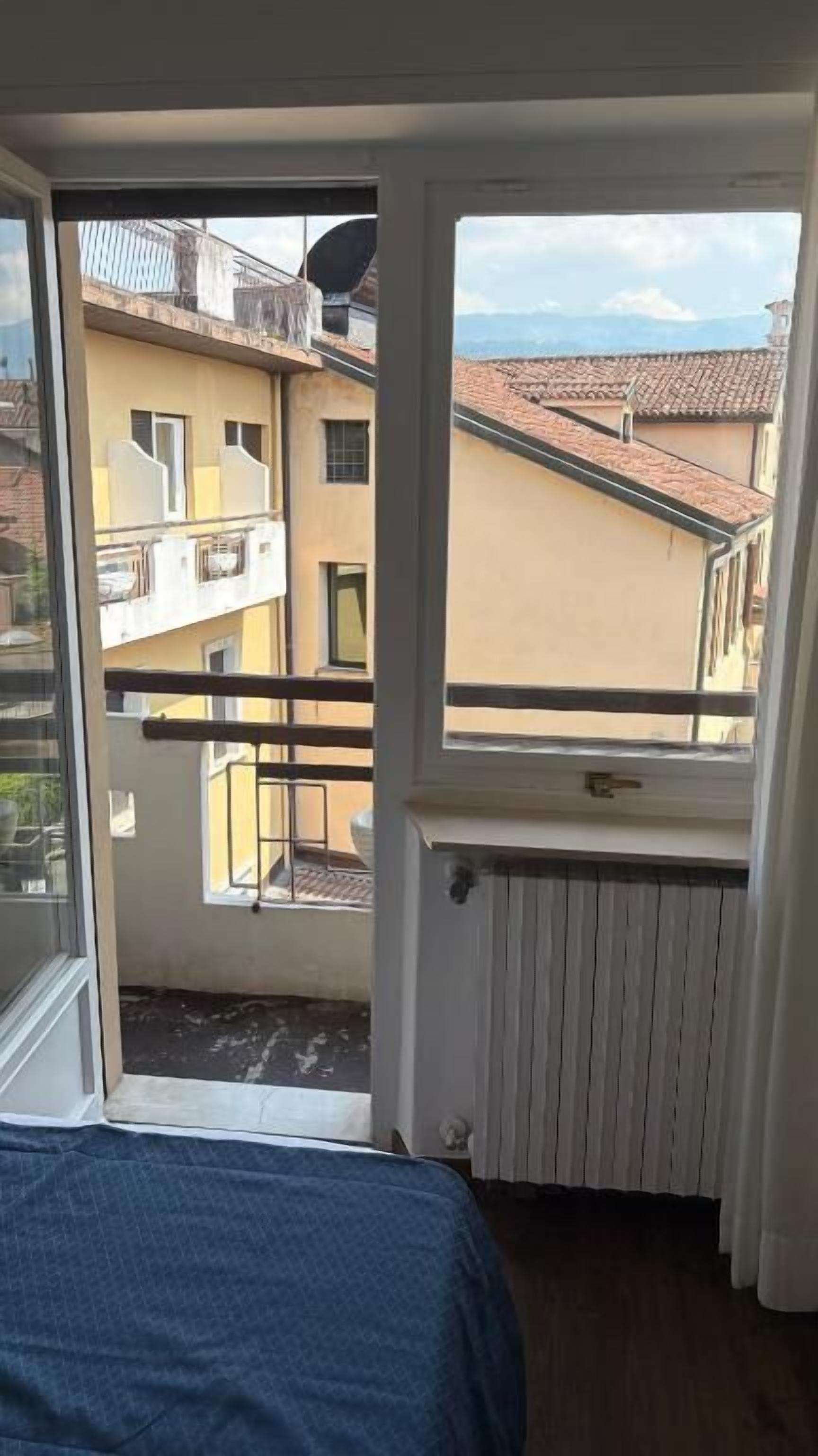 A balcony with a view of neighboring buildings and a window with a view of the sky.
