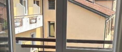 A balcony with a view of neighboring buildings and a window with a view of the sky.