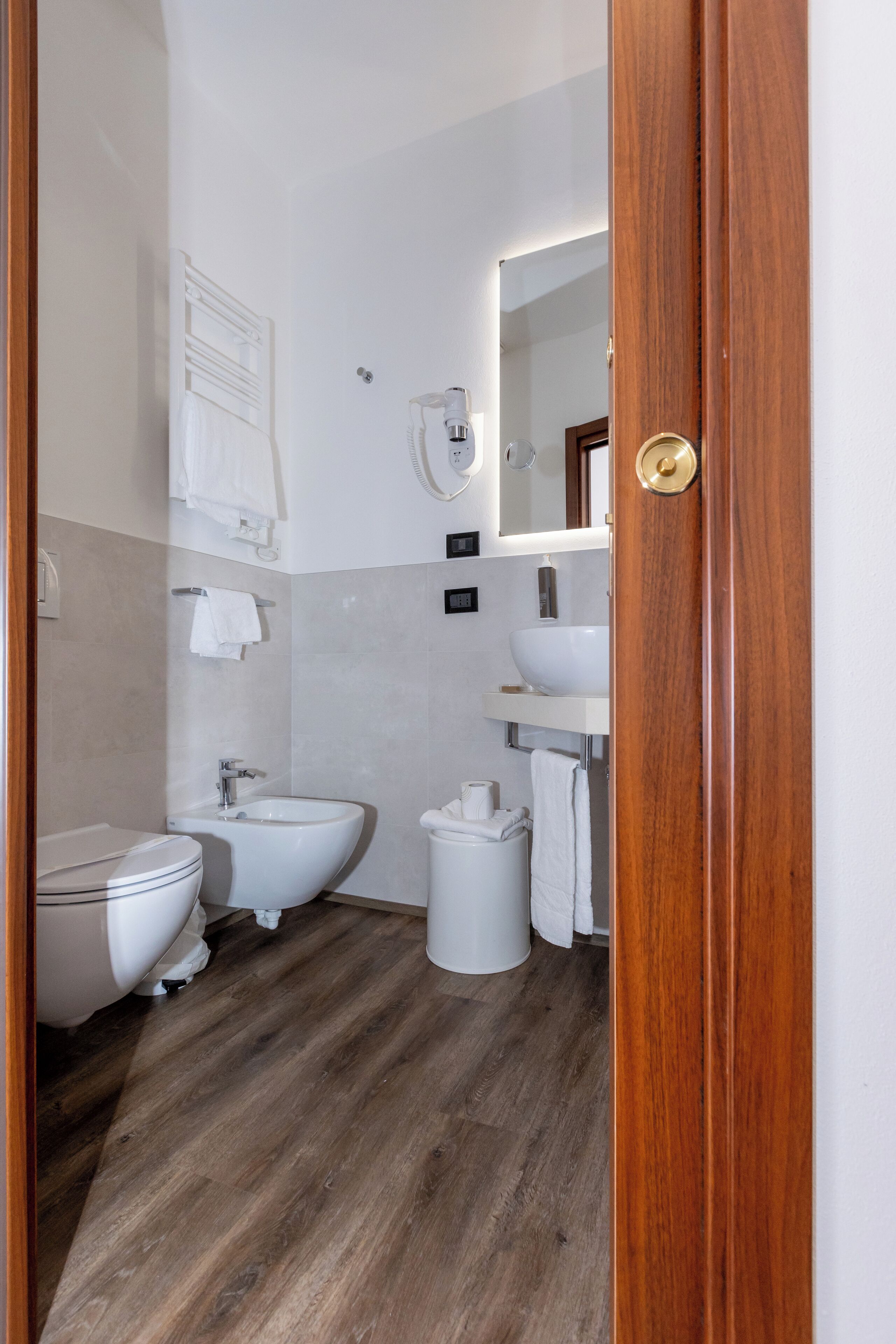 Een badkamer met toilet, bidet en wastafel, houten vloer en een spiegel boven de wastafel.