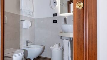 Een badkamer met toilet, bidet en wastafel, houten vloer en een spiegel boven de wastafel.
