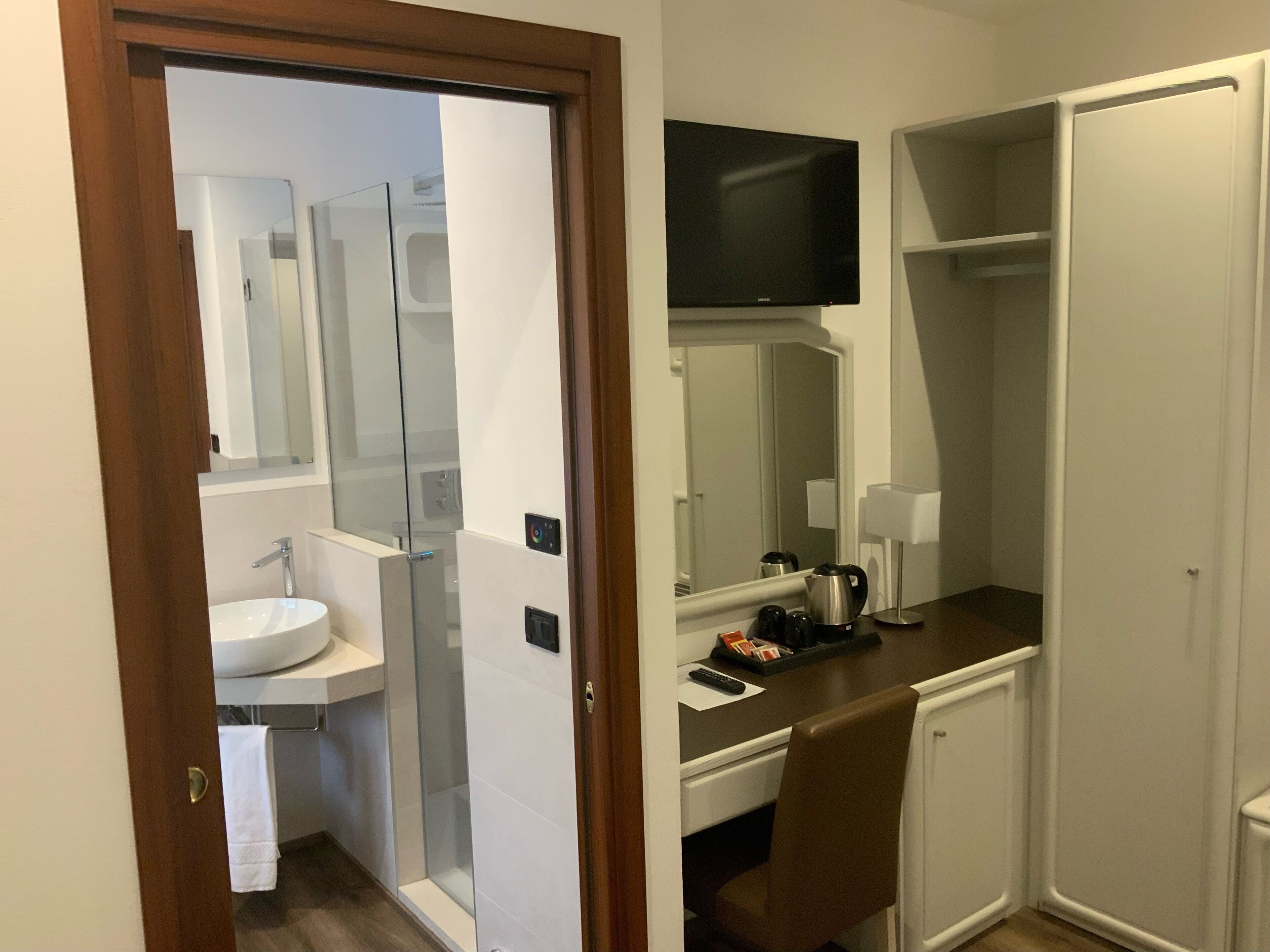A hotel bathroom with a sink, mirror, and a TV mounted above the mirror.
