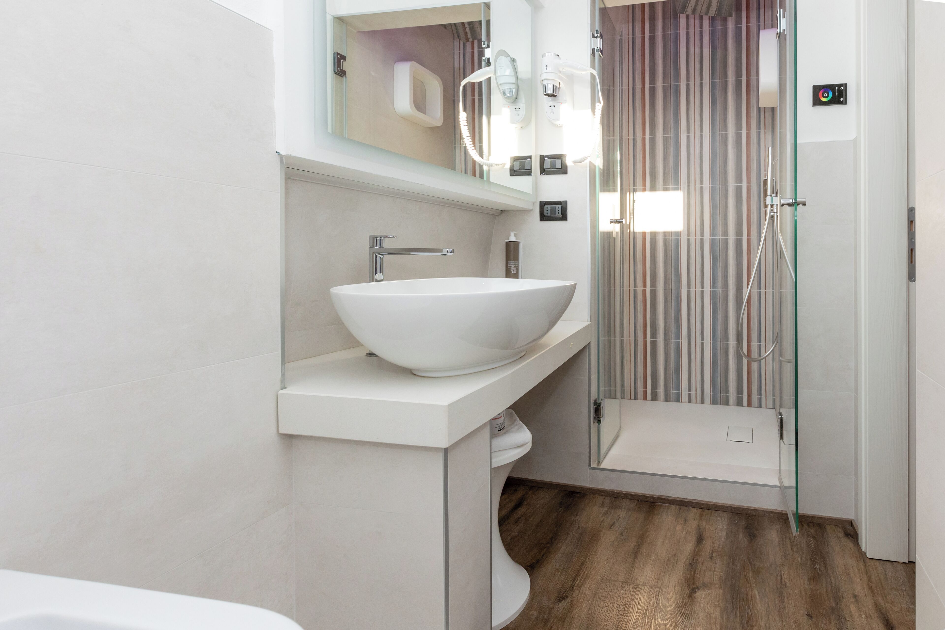 A modern bathroom with a large white sink, a mirror, and a glass shower enclosure.