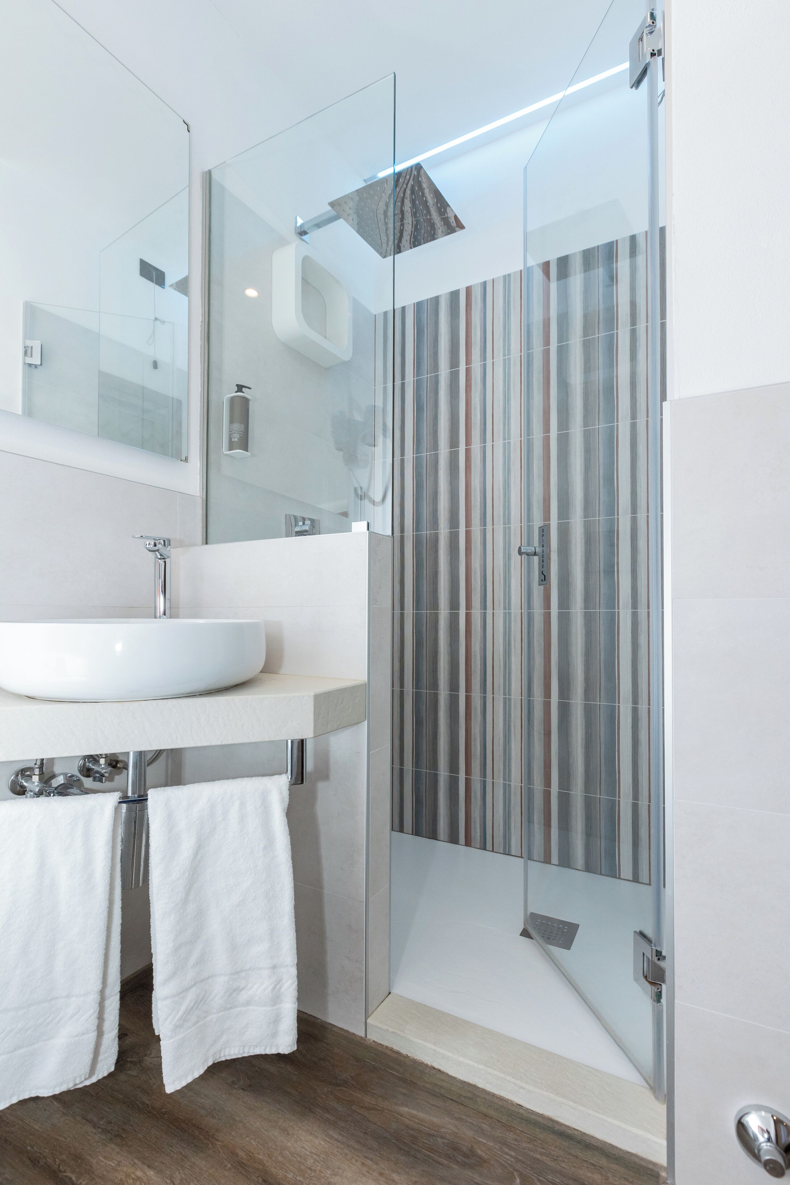 A modern bathroom with a glass-enclosed shower, a white sink, and a large mirror.