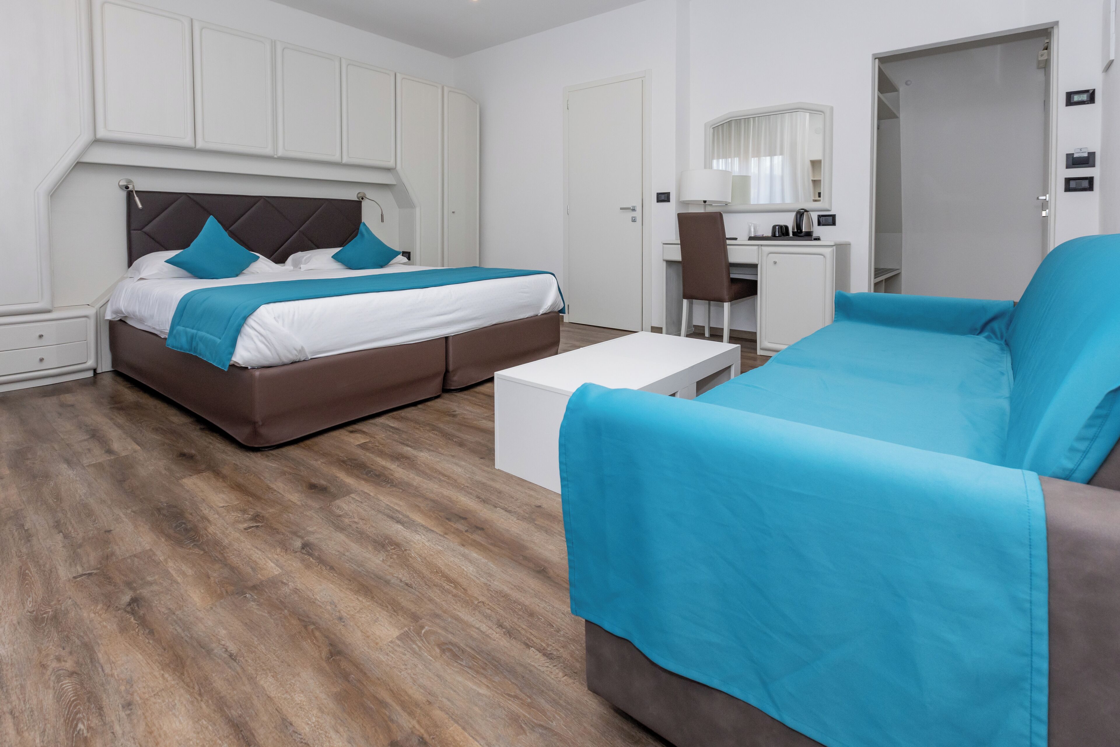 A modern hotel room with a bed, a sofa, a desk, and a chair.
