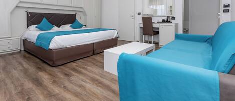 A modern hotel room with a bed, a sofa, a desk, and a chair.
