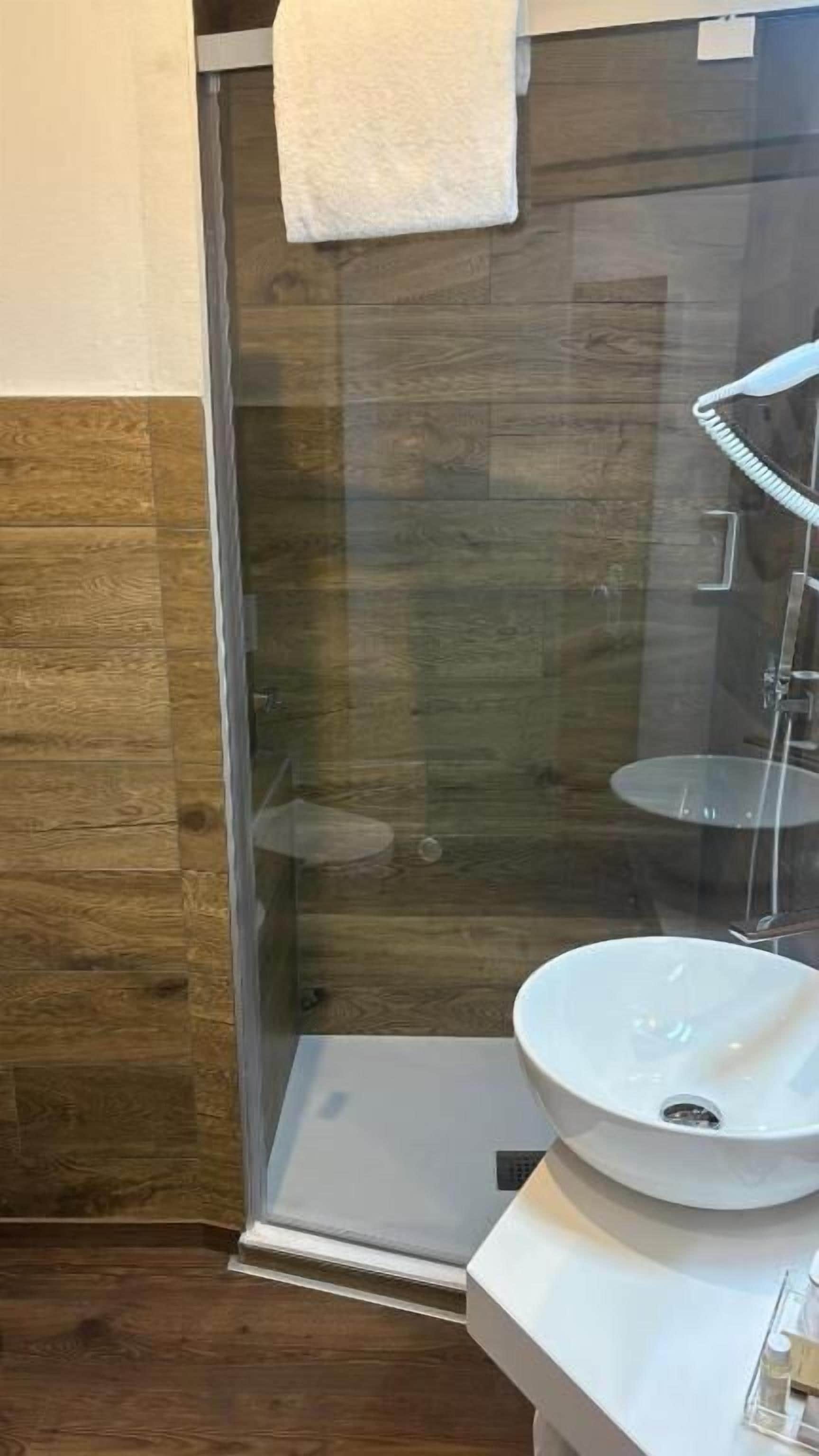 Casa de banho com cabine de chuveiro em vidro, lavatório branco e espelho.