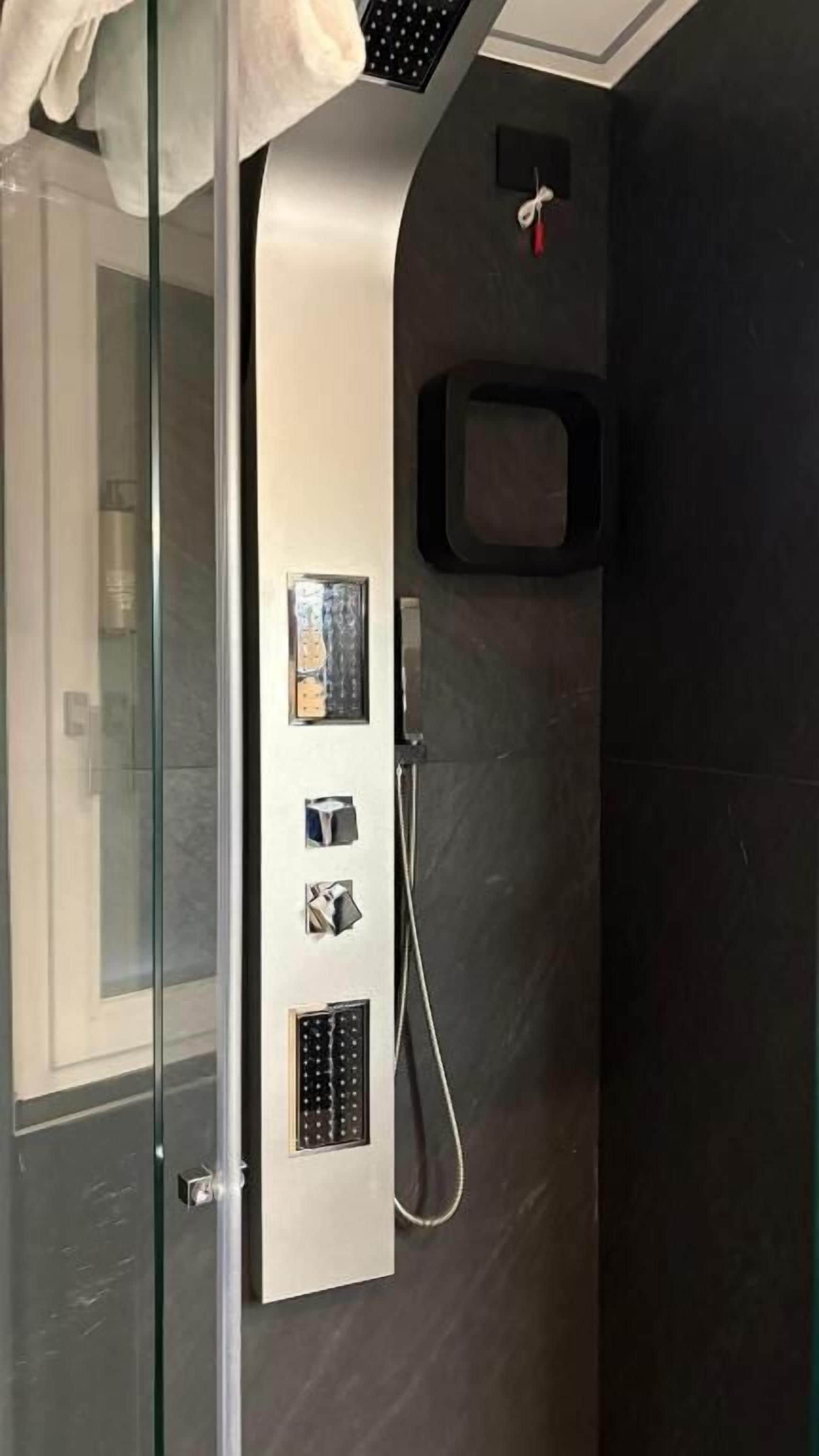 A modern bathroom with a glass shower enclosure, a built-in towel rack, and a wall-mounted control panel.