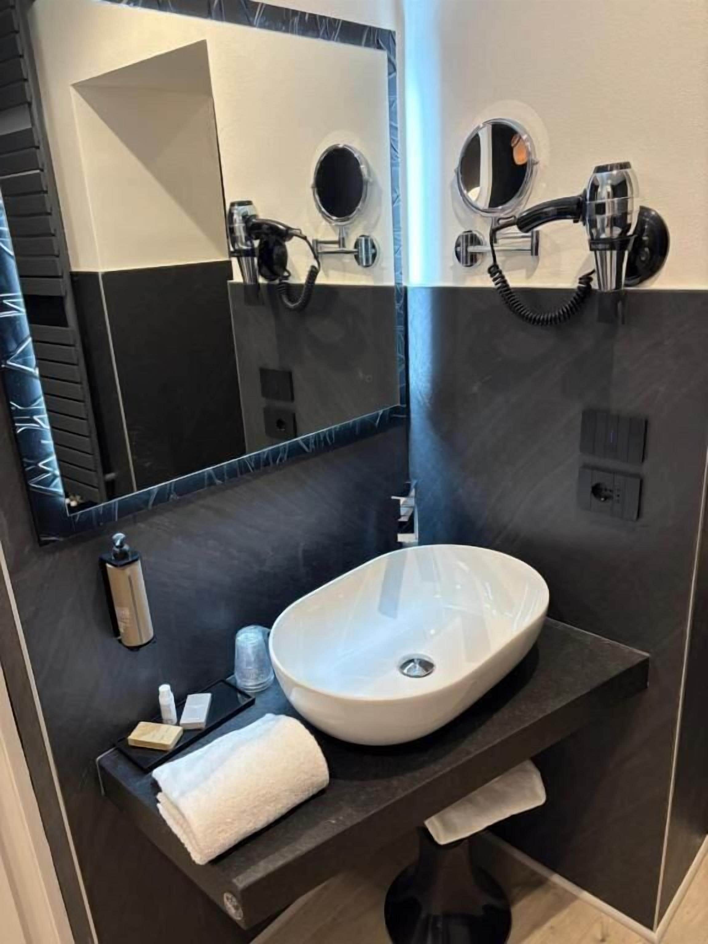Un baño moderno con un lavabo ovalado grande, dos espejos, un perchero y un cabezal de ducha manual.