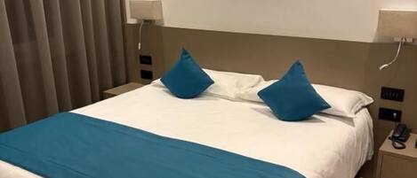 A hotel room with a large bed, two bedside tables, and a curtain on the left.