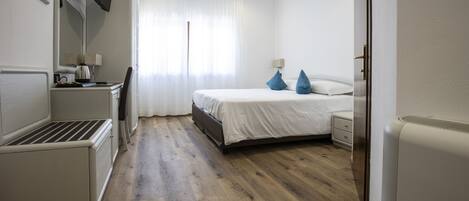 Ein Hotelzimmer mit Bett, Nachttisch, Lampe und einem an der Wand befestigten Flachbildfernseher.