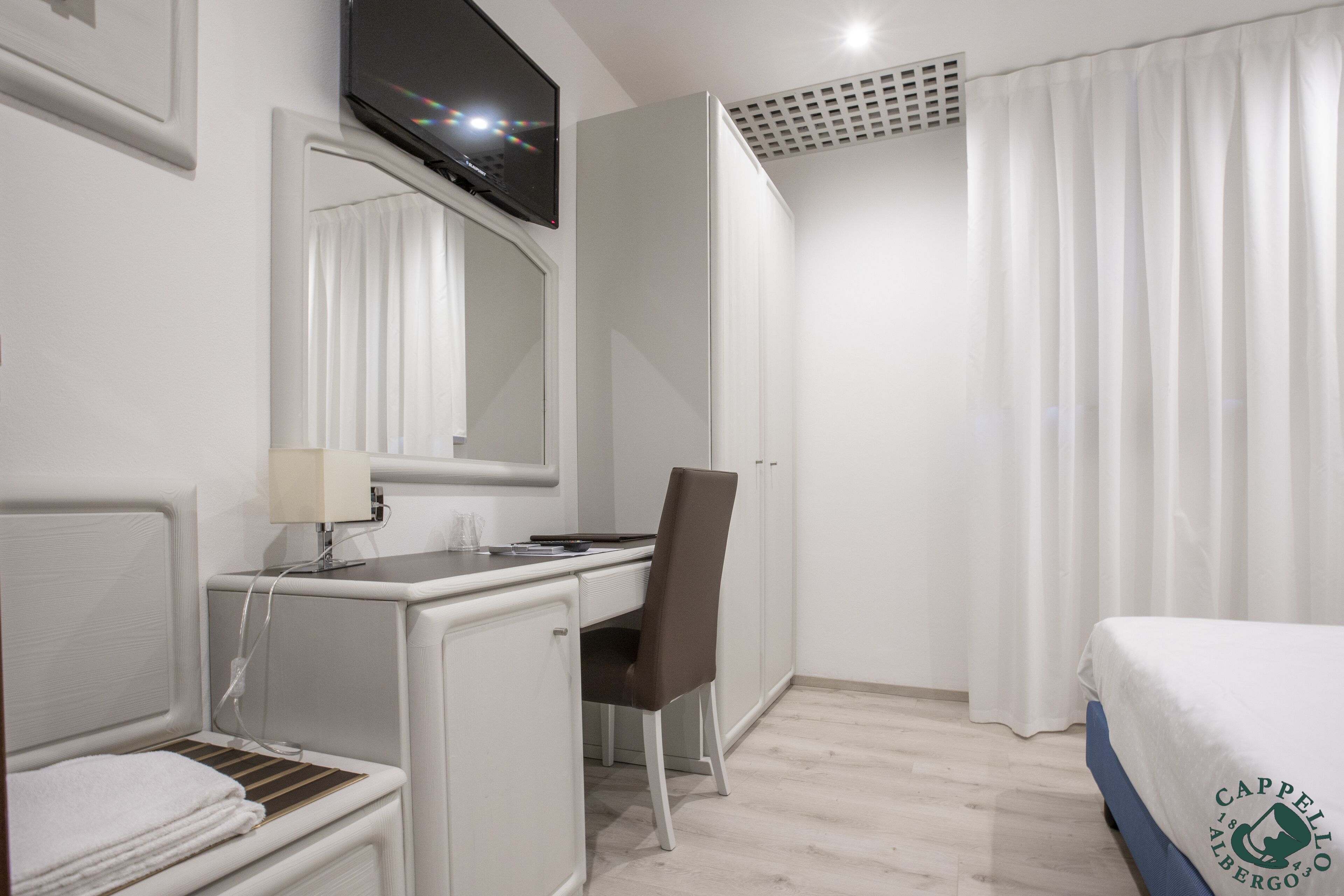 Habitación de hotel con cama, escritorio, silla, televisión y ventana con cortinas.