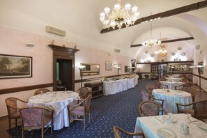 Un comedor con mesas redondas, sillas y candelabros.
