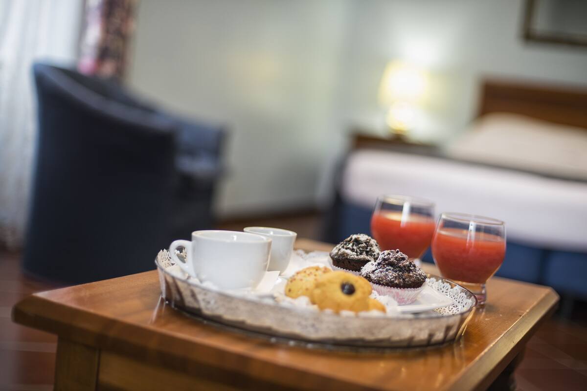Bandeja de desayuno con pasteles y bebidas sobre una mesa de madera en una habitación de hotel.
