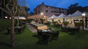 An outdoor dining area with tables and chairs, a fountain, and tents in the background. - La Pineta dei Liberti (Ardea)