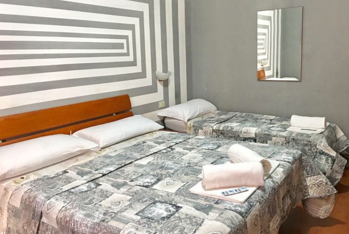 Habitación de hotel con una cama grande, dos camas más pequeñas, cabecera de madera, un espejo y una pared con diseño geométrico.