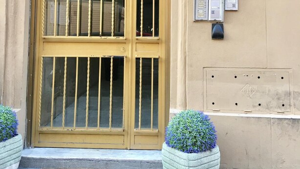 A building entrance with a large wooden door, two potted plants, and several informational signs on the wall.