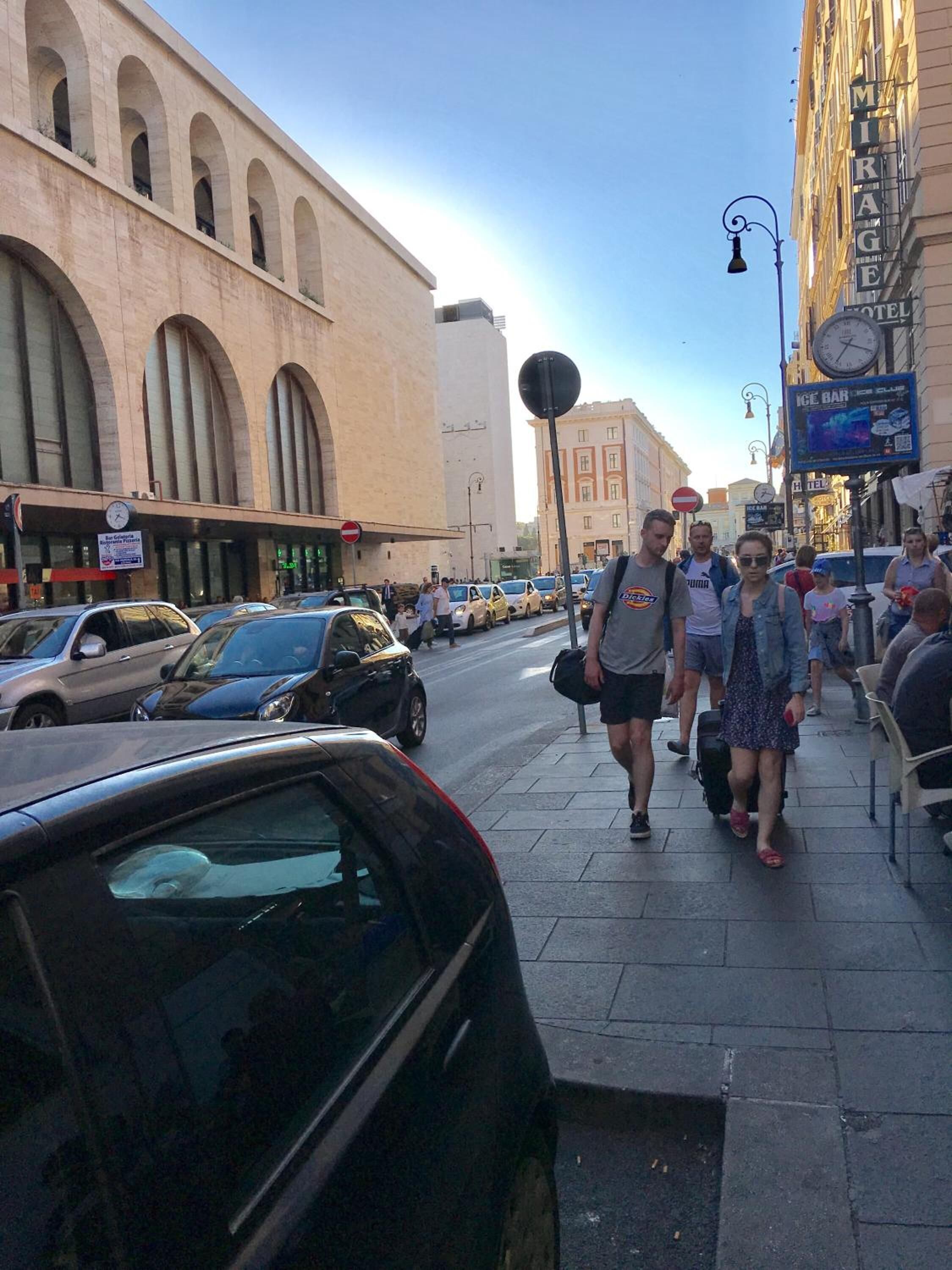A busy street with a building featuring arched windows and a sign for a hotel.