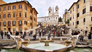 A historic square with a central fountain, a grand staircase leading to a church, and classical architecture.