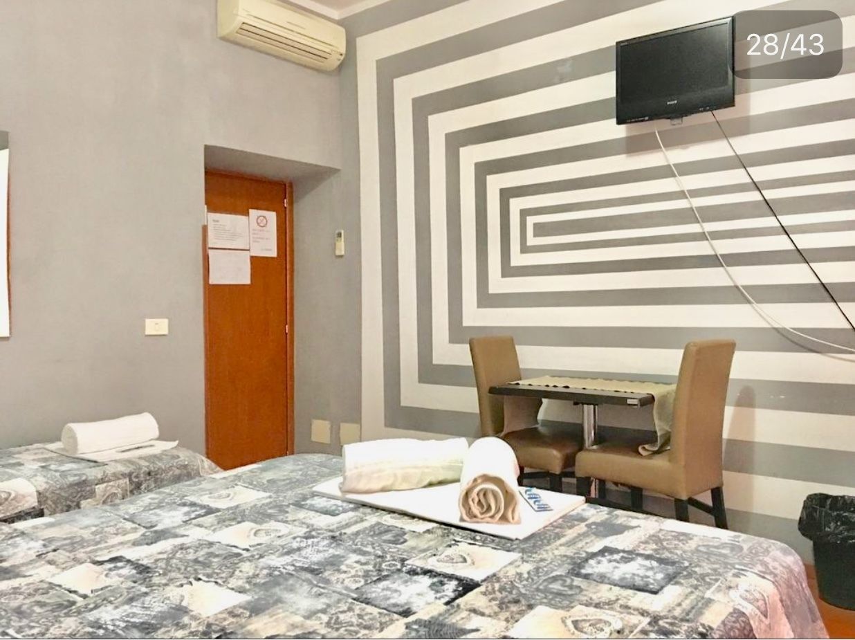 A hotel room with a bed, a desk, two chairs, a TV, and a patterned wall.
